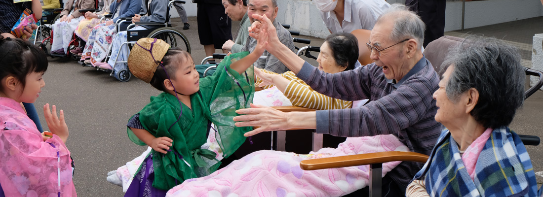 西興部神社例大祭の模様、特養養護老人施設の施設利用者高齢者とお稚児さんがハイタッチをしている画像