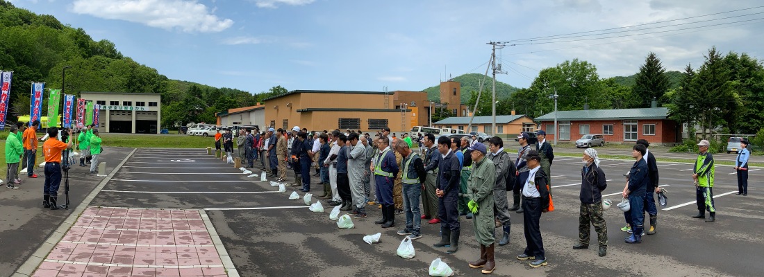 令和7年6月14日土曜日に開催された村民が参加の国道沿線花壇に花を植え美化を目的とした「我が村は美しく事業」の様子。森林公園駐車場に参加者が集まり開会式が行われている様子。